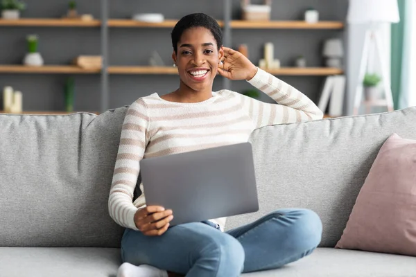 Trabajo remoto. Retrato de la mujer negra feliz sentada en el sofá con el ordenador portátil —  Fotos de Stock