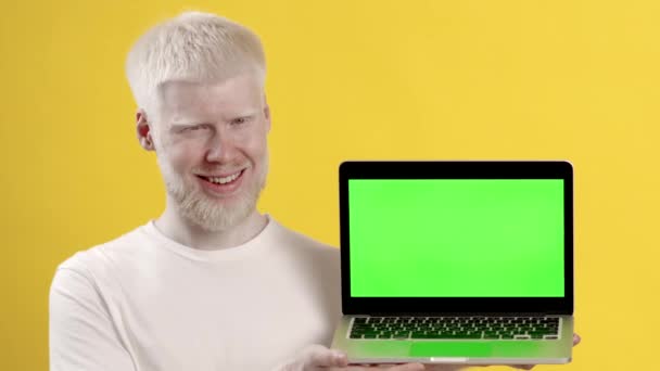 Альбинос человек показывает ноутбук с цветным экраном ключ, желтый фон — стоковое видео