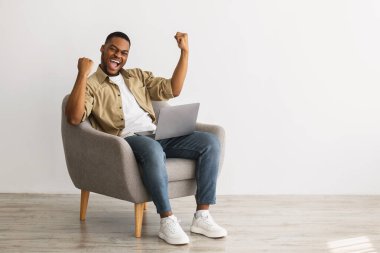 Duygusal Afrikalı Amerikalı Adam dizüstü bilgisayarla başarısını kutluyor. İçeride oturuyor.