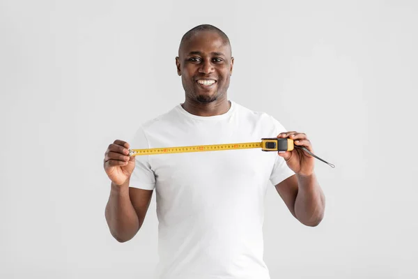 Happy Afro-Amerikaanse klusjesman of bouwer in wit t-shirt met tape-line maatregel en glimlach op de camera — Stockfoto