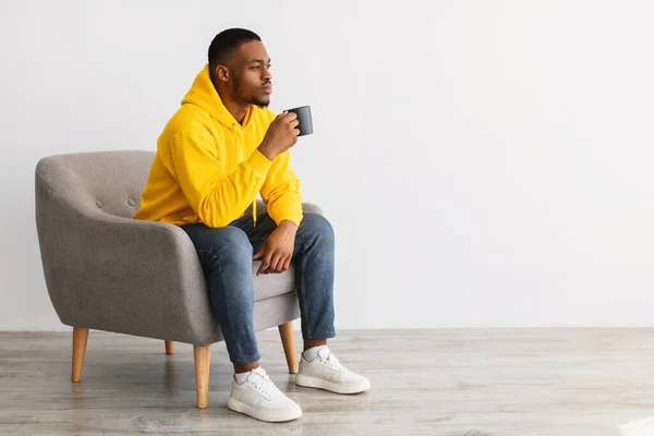 Africano Pensando en beber café sentado sobre fondo gris, Vista lateral —  Fotos de Stock