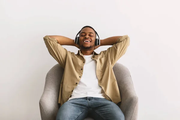 Africano Guy ouvir música relaxante sentado em poltrona, fundo cinza — Fotografia de Stock