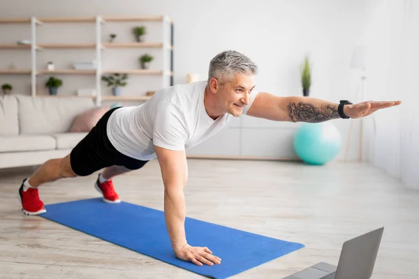 Çevrimiçi yerel spor. Üst düzey bir adam dizüstü bilgisayarda video çalışıyor, tahta yapıyor ve bir kolunu kaldırıyor. — Stok fotoğraf