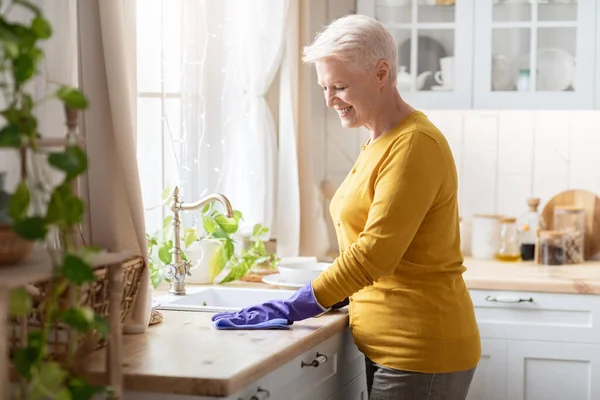 漂亮的老太太在厨房里打扫卫生，戴着橡胶手套 — 图库照片