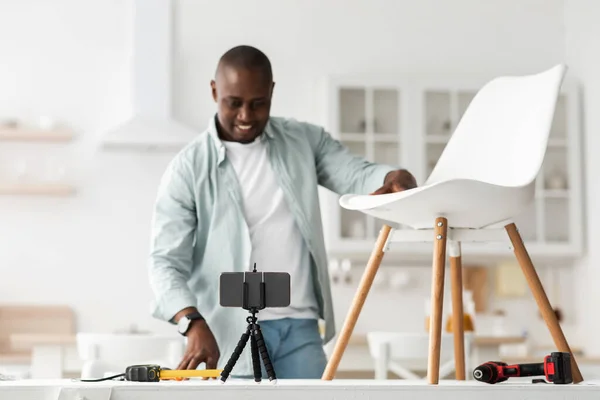 Blogger moderno. Feliz hombre negro mostrando su silla ya hecha y mirando a la cámara del teléfono inteligente, grabación de vídeo — Foto de Stock