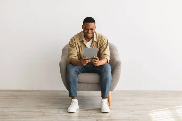 Hombre africano feliz usando tableta digital sentado sobre fondo gris —  Fotos de Stock