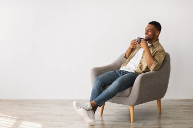 Rahat siyah adam kahvesini içiyor Gri sandalyesinde oturuyor