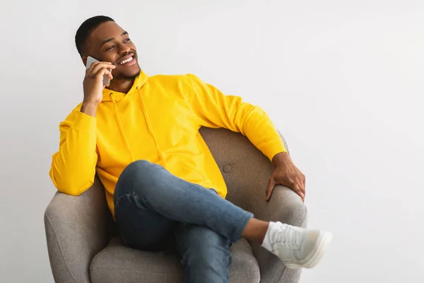 Alegre negro chico hablando en teléfono sentado sobre gris fondo —  Fotos de Stock