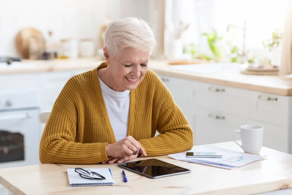 Fröhliche grauhaarige Seniorin nutzt digitales Tablet in Küche — Stockfoto