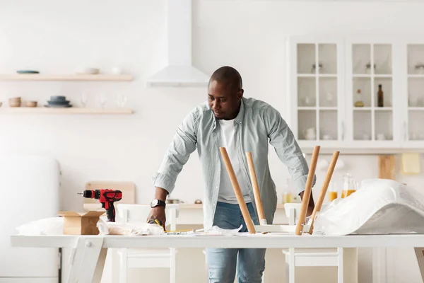 Hombre negro instalando silla de madera después de la reubicación del hogar. Manitas serios listos para trabajar con taladro y herramientas electicas — Foto de Stock