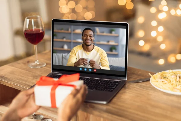 Young black woman having online date with her boyfriend or husband, showing wrapped gift box at laptop screen — Stock Photo, Image