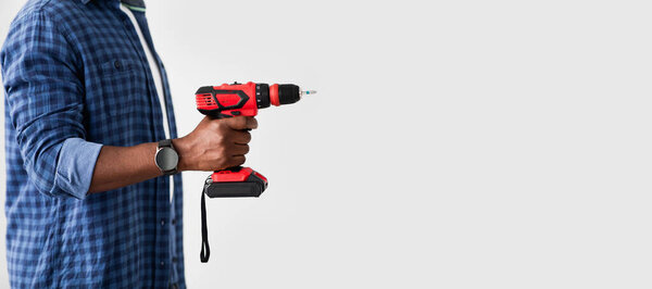 Black man with smartwatch holding electric drill, ready to repair home furniture, side view, panorama with empty space