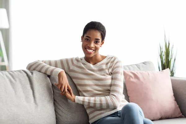 Jong gelukkig Afrikaans amerikaans huisvrouw zitten op bank in woonkamer — Stockfoto