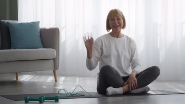 Sportig äldre kvinna vinka hand ler mot kameran hemma — Stockvideo
