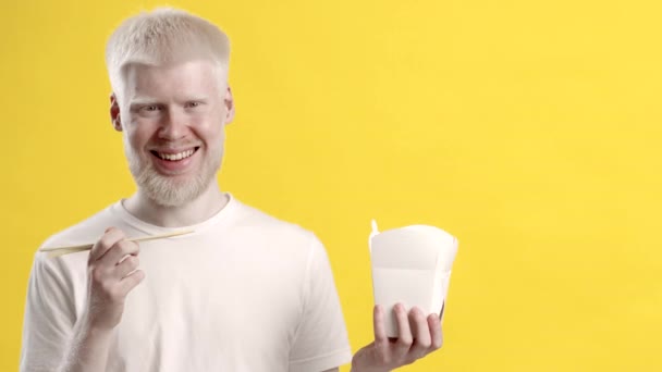 Альбіно людина показує паперову обідню коробку стоячи на жовтому тлі — стокове відео