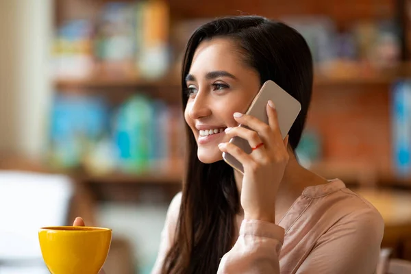 Kahve içerken ve kafeteryada tek başına vakit geçirirken akıllı telefondan konuşan mutlu Latin bayan. — Stok fotoğraf