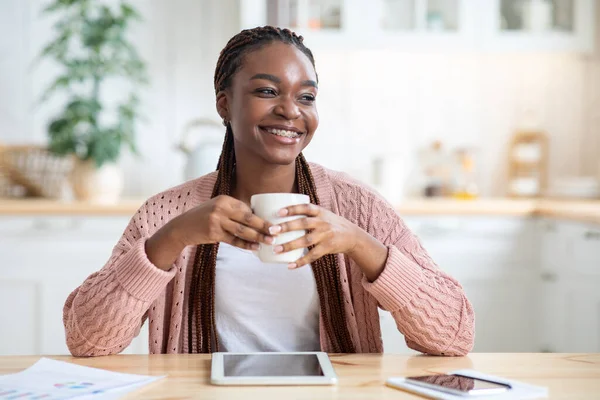 Relaxado mulher negra sentada na mesa na cozinha e beber café — Fotografia de Stock