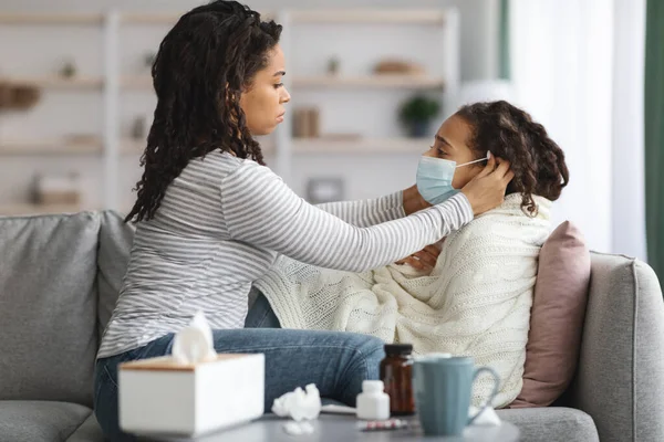 Madre negra poniendo mascarilla en su pequeña hija enferma —  Fotos de Stock