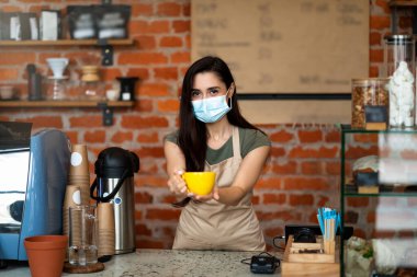 Kendi kafeteryasında misafirleri karşılayan mutlu barista, bir fincan sıcak içecek sunuyor, covid-19 salgınından sonra işe geri dönüyor.