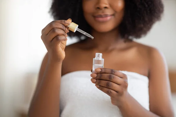 Vista cortada de jovem mulher negra em toalha de banho aplicando soro facial dentro de casa, close-up — Fotografia de Stock