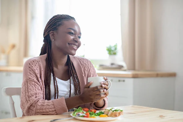 Morning Relax. Happy African Woman Drinking Coffee While Having Breakfast In Kitchen