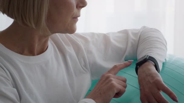 Onherkenbare senior vrouw met behulp van Smartwatch tijdens het sporten binnen zitten — Stockvideo