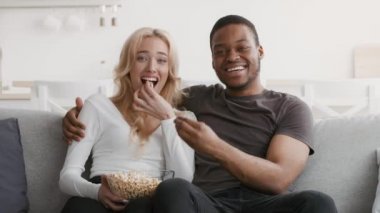 Çeşitli çiftler TV izlerken gülüyor ve evde patlamış mısır yiyor.