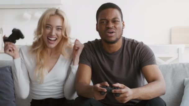 Diversa pareja jugando videojuego divirtiéndose sentada en casa — Vídeo de stock