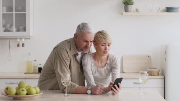 Ontevreden Middeleeuws paar met behulp van Smartphone Scrolling Negatief nieuws in de keuken — Stockvideo