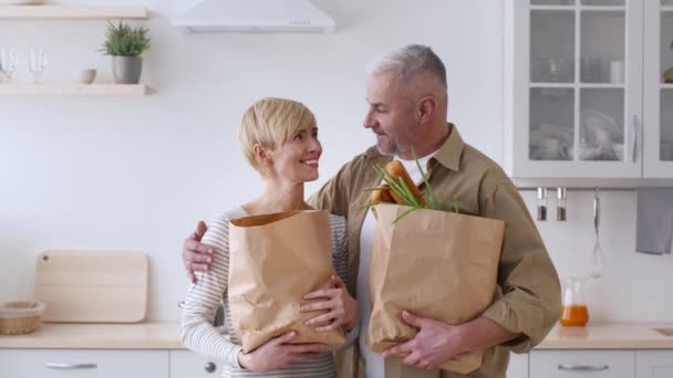 Familia feliz pareja posando sosteniendo bolsas de compras de comestibles en la cocina — Vídeos de Stock