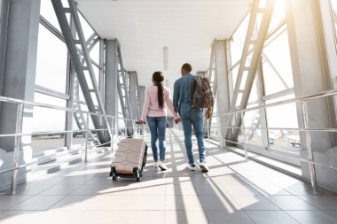 Tatil gezisi. Siyah bir çiftin havalimanında Bavulla yürüyüşünün arka görüntüsü