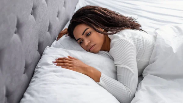 Deprimida senhora negra deitada na cama sozinha e se sentindo chateada — Fotografia de Stock
