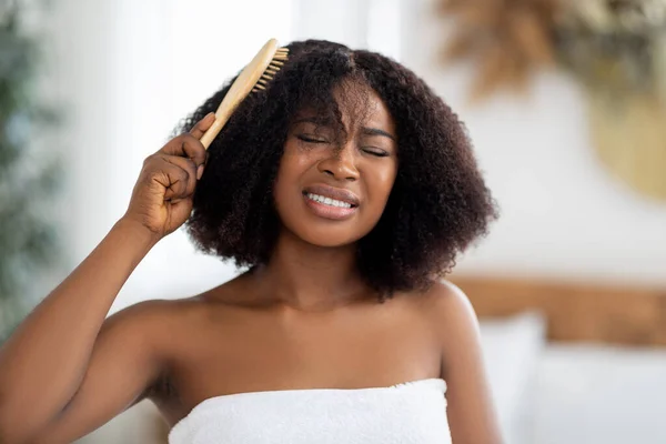 Wanita kulit hitam milenial yang frustrasi mencoba menyikat rambutnya yang kusut di rumah. Konsep tata rambut dalam negeri — Stok Foto