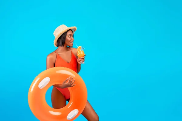 Refroidir l'été. Cool femme noire en maillot de bain tenant anneau gonflable et cocktail de fruits à boire sur fond bleu — Photo