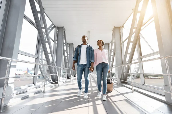 Viajando juntos. Alegre pareja negra sosteniendo manos mientras camina en la terminal del aeropuerto — Foto de Stock