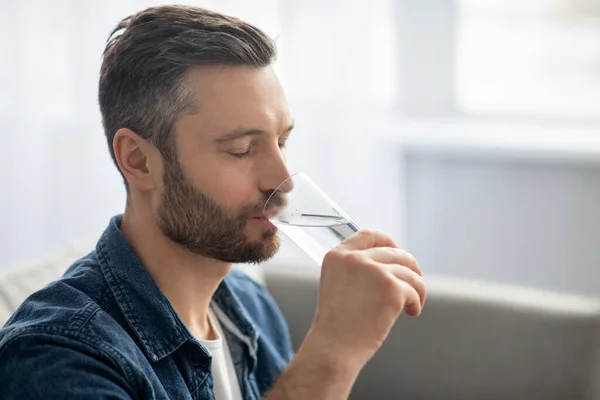 수염을 기른 사람 이 집에서 물을 마시고 있는 모습, 옆을 바라봄 — 스톡 사진