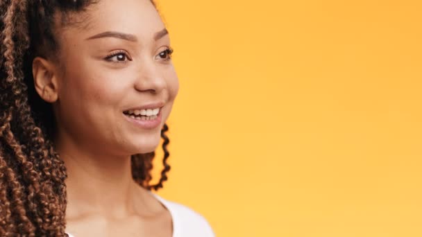 Positiva alegre joven afroamericana feliz dama mirando a un lado y sonriendo, fondo naranja, espacio vacío — Vídeo de stock