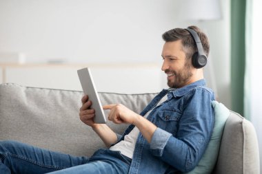 Kulaklık ve dijital tabletli pozitif sakallı adam.