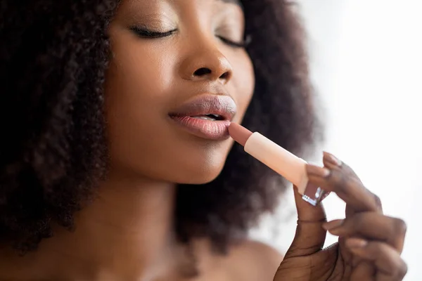 Potret closeup dari wanita hitam muda mengoleskan lipstik dengan mata tertutup, merawat penampilannya di dalam ruangan — Stok Foto