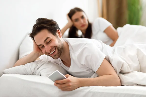 Fusk make sms: a på telefon Ignorera fru ligger i sängen — Stockfoto