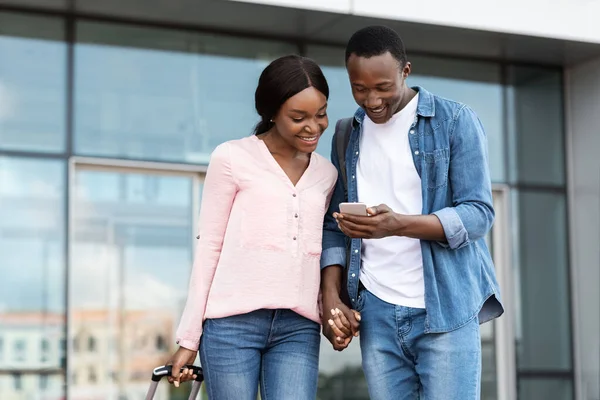 Cartes de ville en ligne. Couple noir heureux en utilisant Smartphone en plein air près du terminal de l'aéroport — Photo