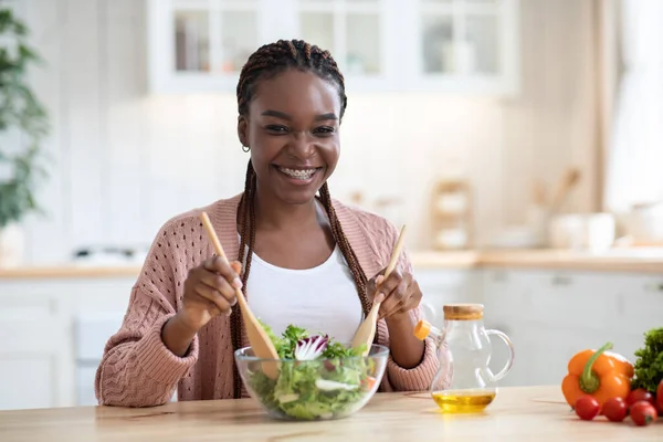 Feliz sonriente mujer afroamericana preparando ensalada de verduras frescas en la cocina —  Fotos de Stock