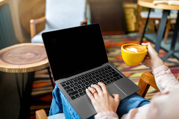 Ugjenkjennelig dame som skriver på en bærbar datamaskin med tom skjerm, bilde med kopirom, sittende på en kafe – stockfoto
