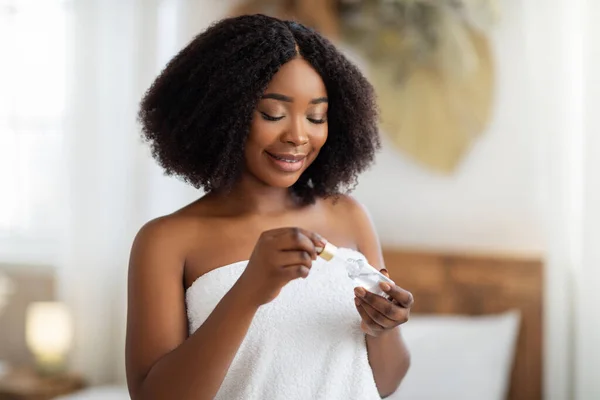 Atractiva dama afroamericana con piel brillante saludable aplicando suero facial hidratante en casa — Foto de Stock