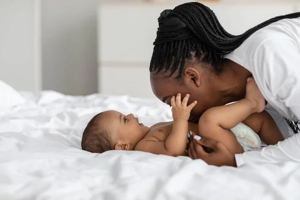 Svart mamma leker med sitt spädbarn, kysser barnet i magen — Stockfoto