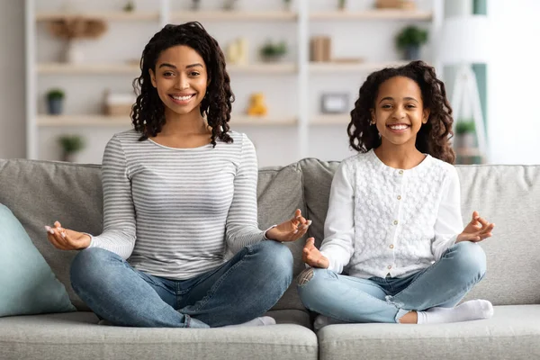 Vidám fekete anya és lánya ül a kanapén, meditál — Stock Fotó