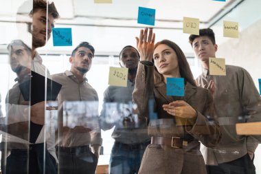 İş arkadaşları cam duvardaki yapışkan yapışkan yapışkan yapışkan yapışkan not kağıtlarını kullanarak toplantı yapıyorlar.