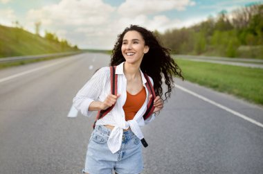 Sırt çantalı güzel bir kadın otobanda yürüyor, otostop ile seyahat ediyor, kırsalda otostop çekiyor.
