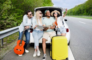 Arabayla seyahat eden, haritayı kontrol eden, akıllı telefondan selfie çeken, dışarıda eğlenen çok kültürlü arkadaşlar.