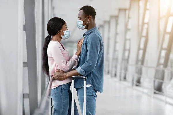 Feliz Reunión. Pareja negra feliz en las máscaras médicas protectoras que abrazan en aeropuerto —  Fotos de Stock